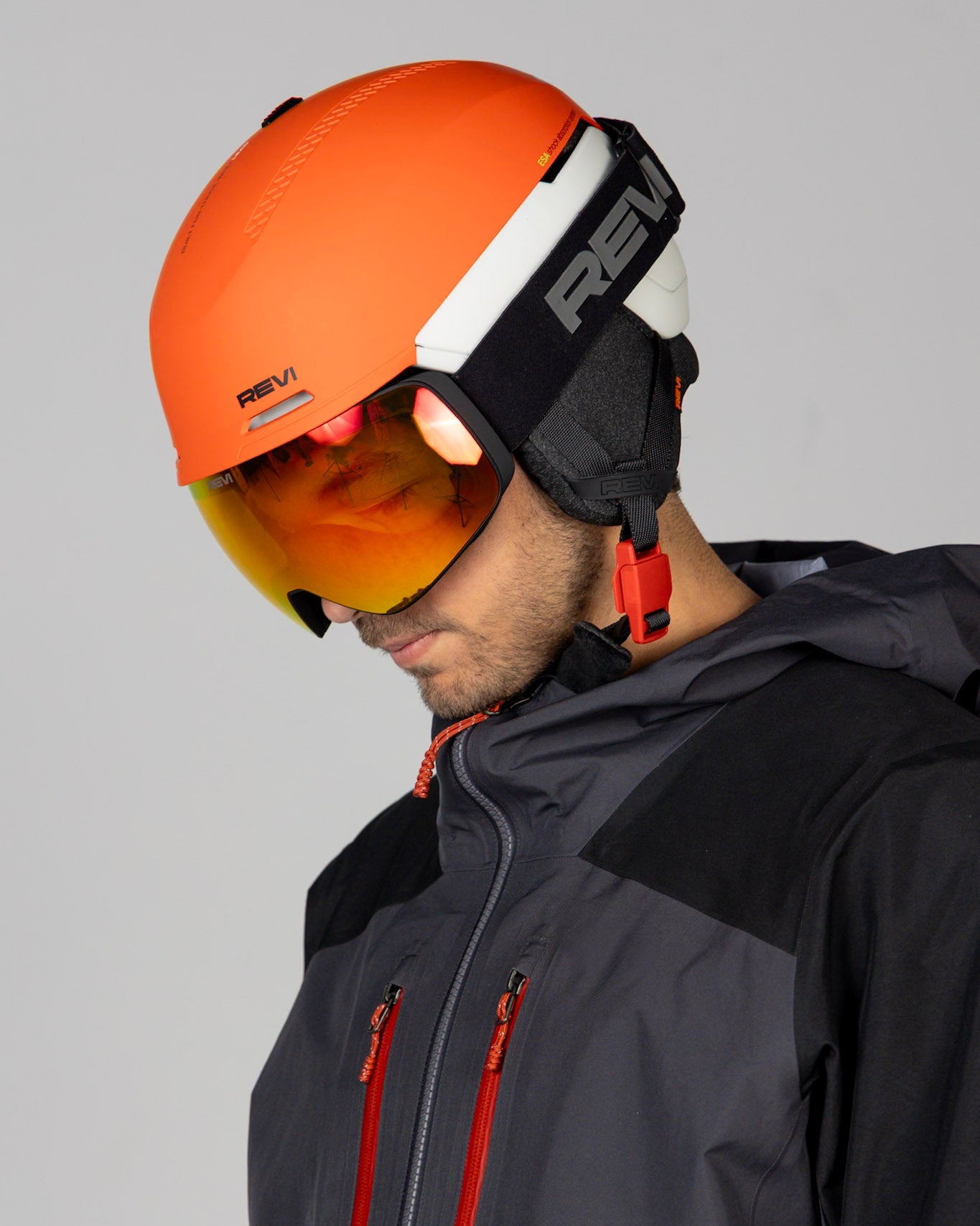 Person wearing an orange helmet and black jacket with red accents on a gray background