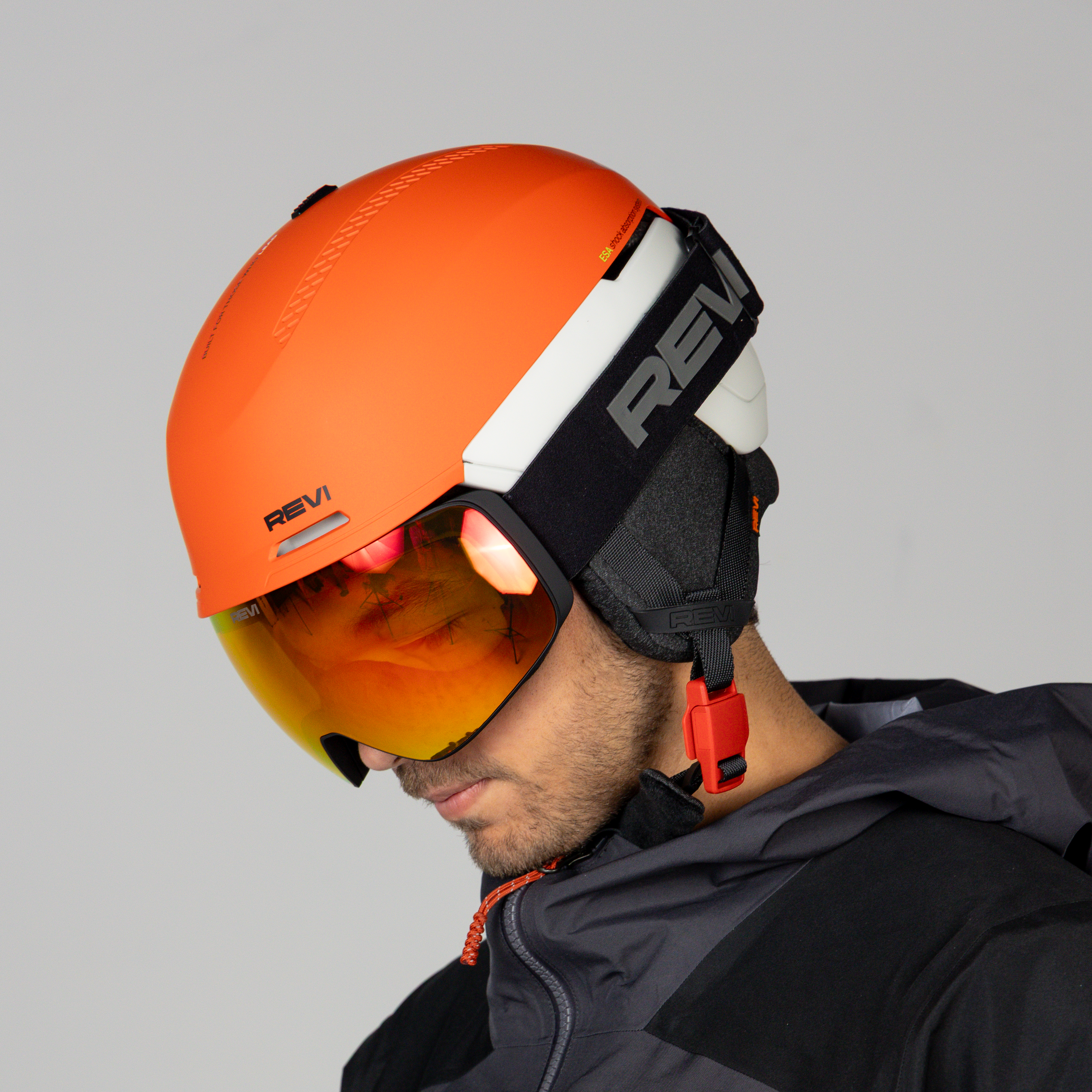 Person wearing an orange helmet with a brand logo and reflective goggles on a gray background