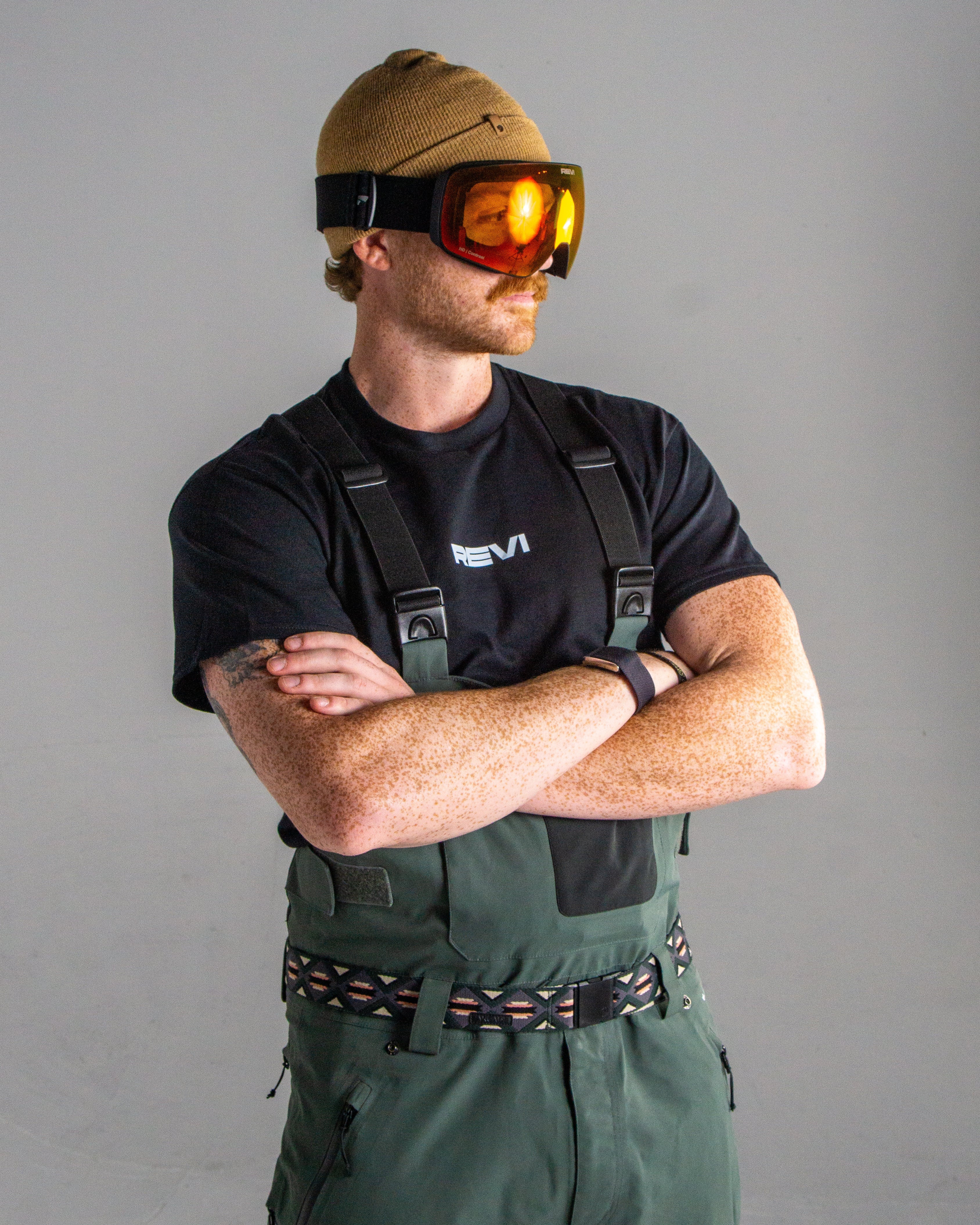 Person wearing a black shirt, green overalls, and goggles on a gray background